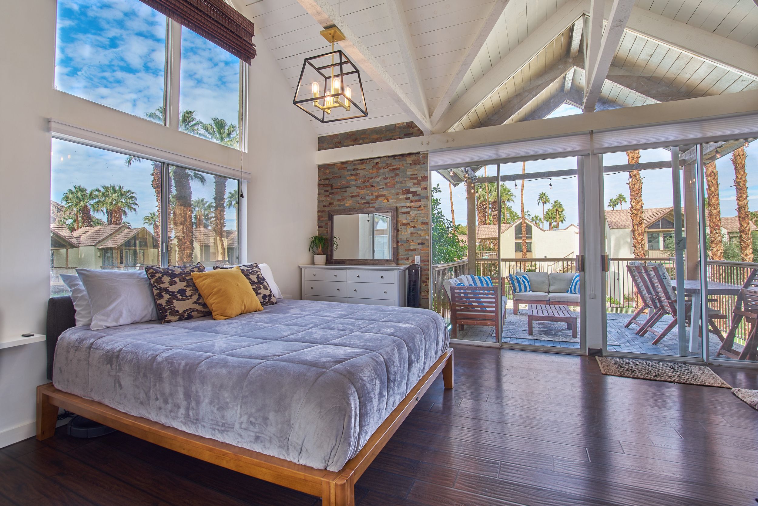 Luxurious bedroom with high ceilings and sliding glass doors opening to a balcony with palm tree views.