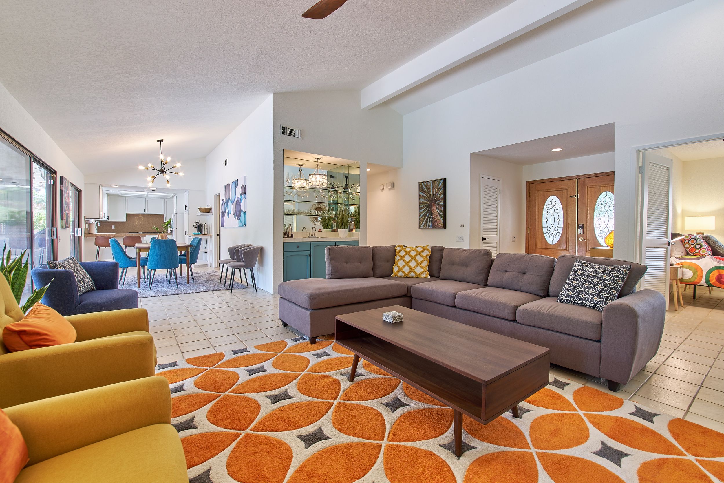 Modern living room with gray sectional sofa and vibrant orange geometric rug creating a stylish space.