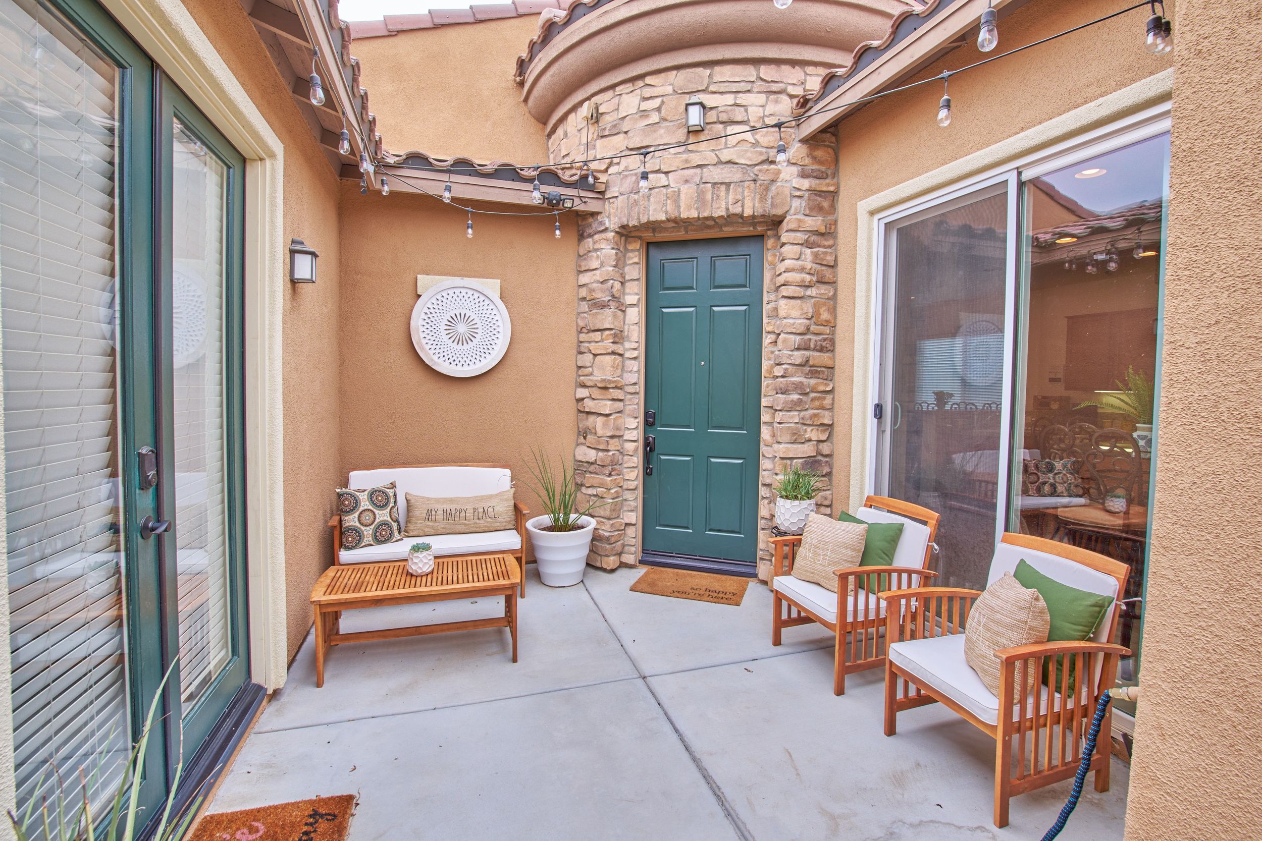 Cozy outdoor patio space with stone accent wall, wooden furniture, and teal door entrance.