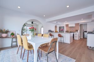 Bright open concept dining area and kitchen with modern white furniture and natural wood floors.