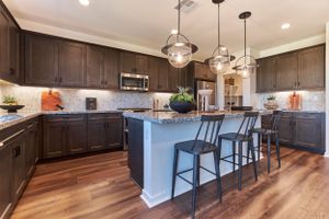 Modern kitchen with dark wood cabinets, center island, pendant lighting, and hardwood floors.