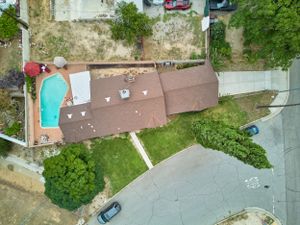 Drone shot of a residential property with a brown roof and backyard swimming pool viewed from above.