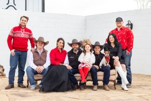Family group photo of nine people wearing cowboy hats and holiday attire seated outdoors on a patio.