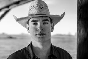 Black and white close-up portrait of young man in straw cowboy hat outdoors.