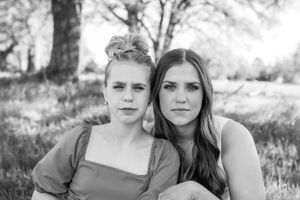 Black and white portrait of two young women sitting close together under a tree.
