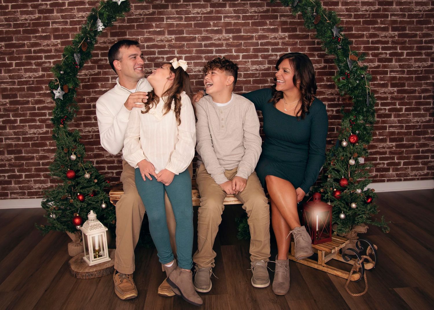 Holiday family portrait with festive greenery arch and brick wall background.