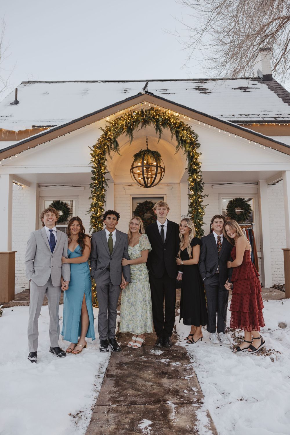 Formal group photo outside snow-covered building with holiday wreath and lights.