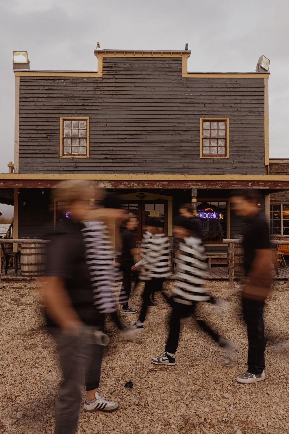 Motion blur captures people in striped clothing moving past old western building facade.