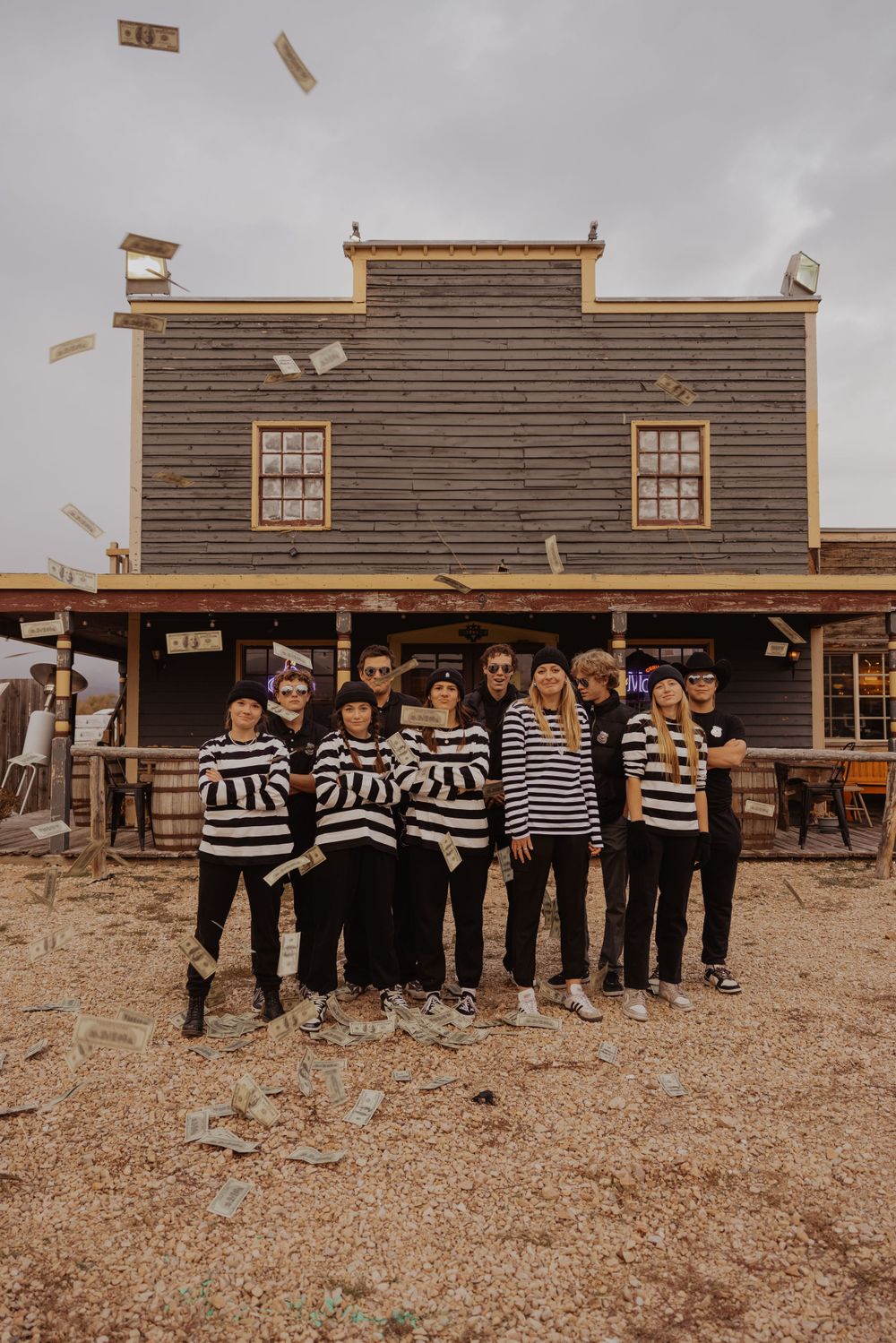 Group photo of performers in mixed stripes and dark clothing in front of rustic western building.
