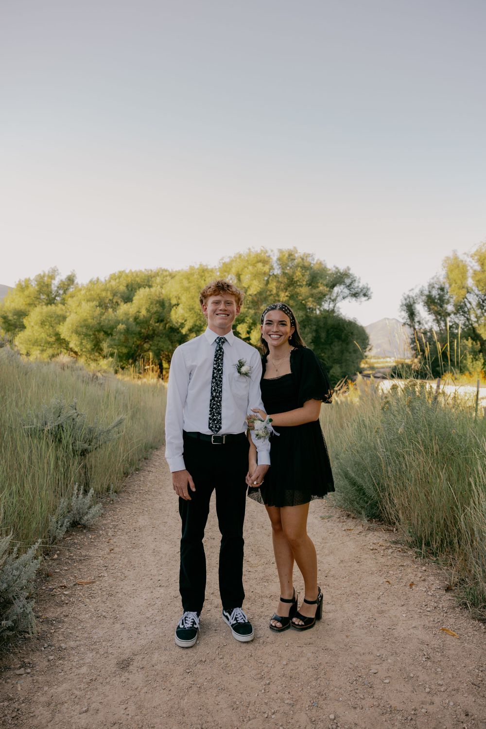 A formal couple poses together on a nature trail during golden hour.
