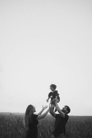 Parents lifting child in field against minimalist white sky.