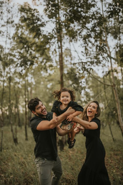 A happy family playing and lifting their child in a wooded area during golden hour.