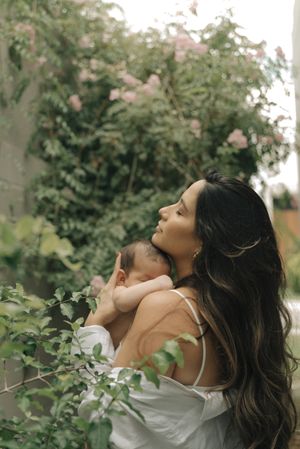 Parent holding baby against flowering bushes in a dreamy outdoor garden setting.