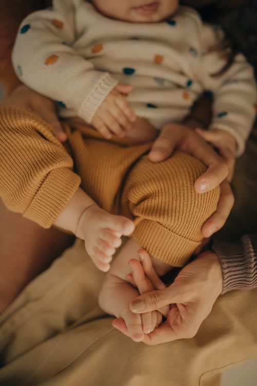 Close-up of tiny baby feet and hands being held in polka dot onesie.