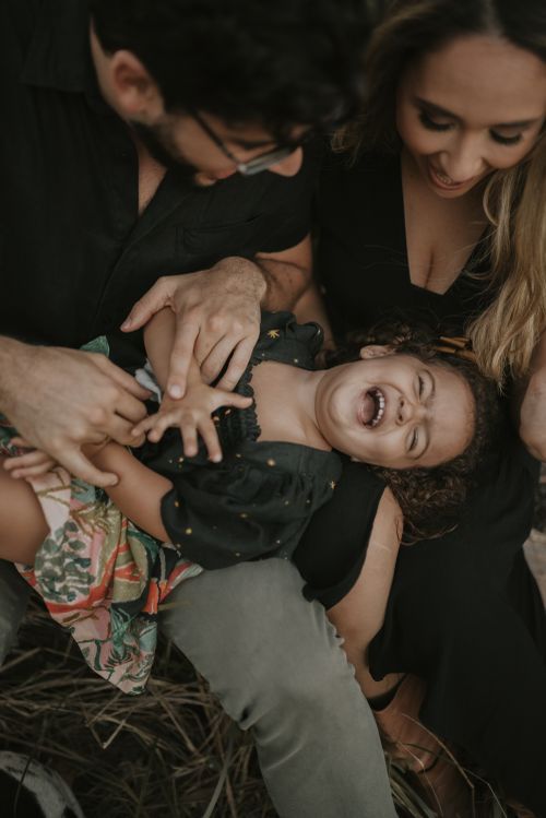 Parents playfully tickling their laughing child during an outdoor photo session.
