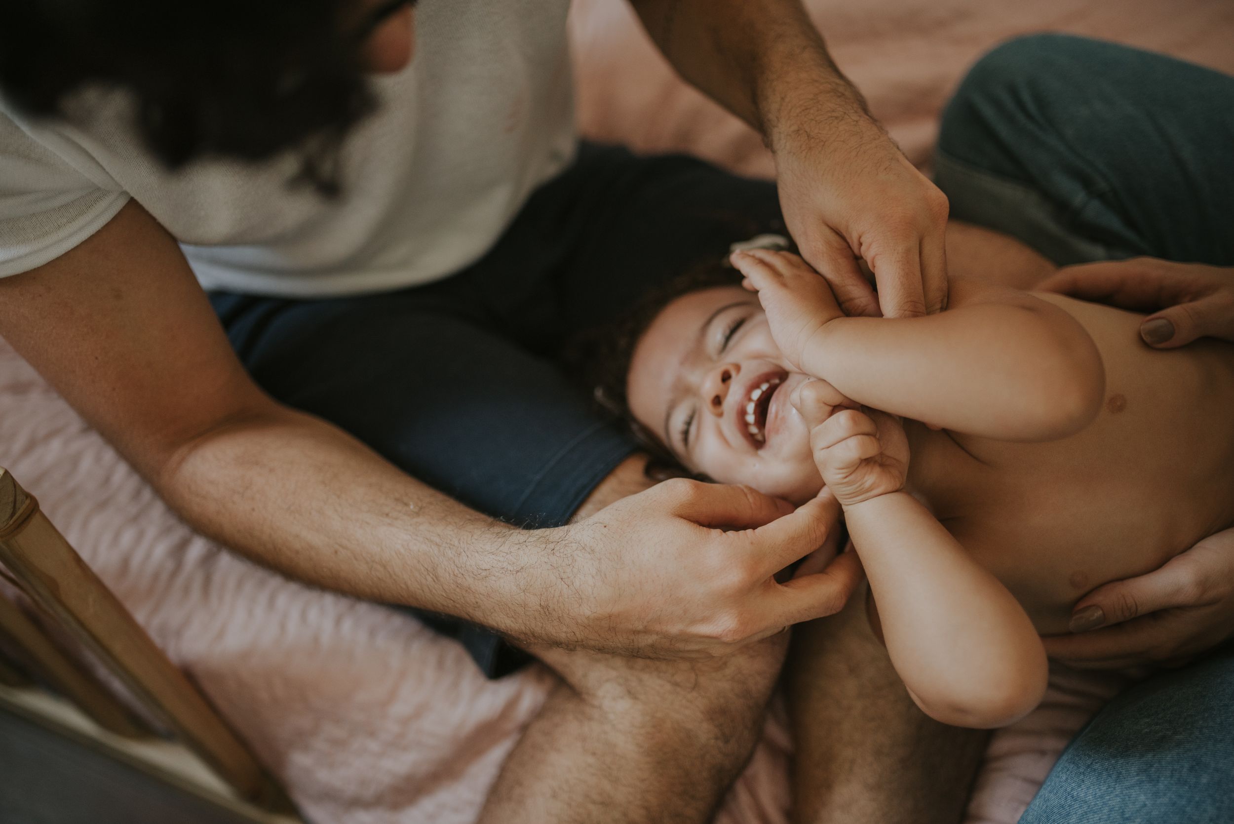 An intimate closeup of parents playing with their giggling baby on a comfortable surface.