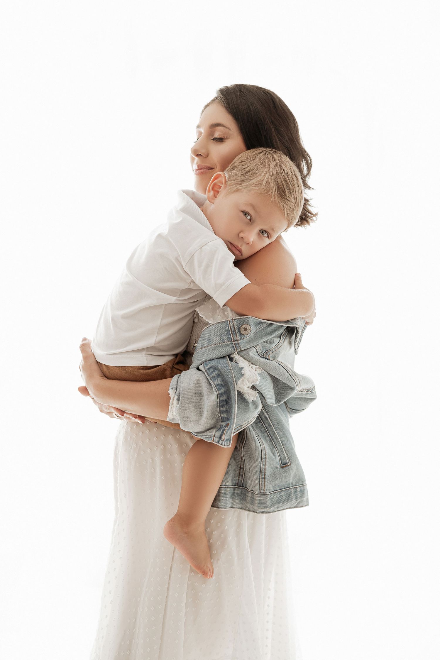 Tender moment between mother and child as they embrace in white studio setting.
