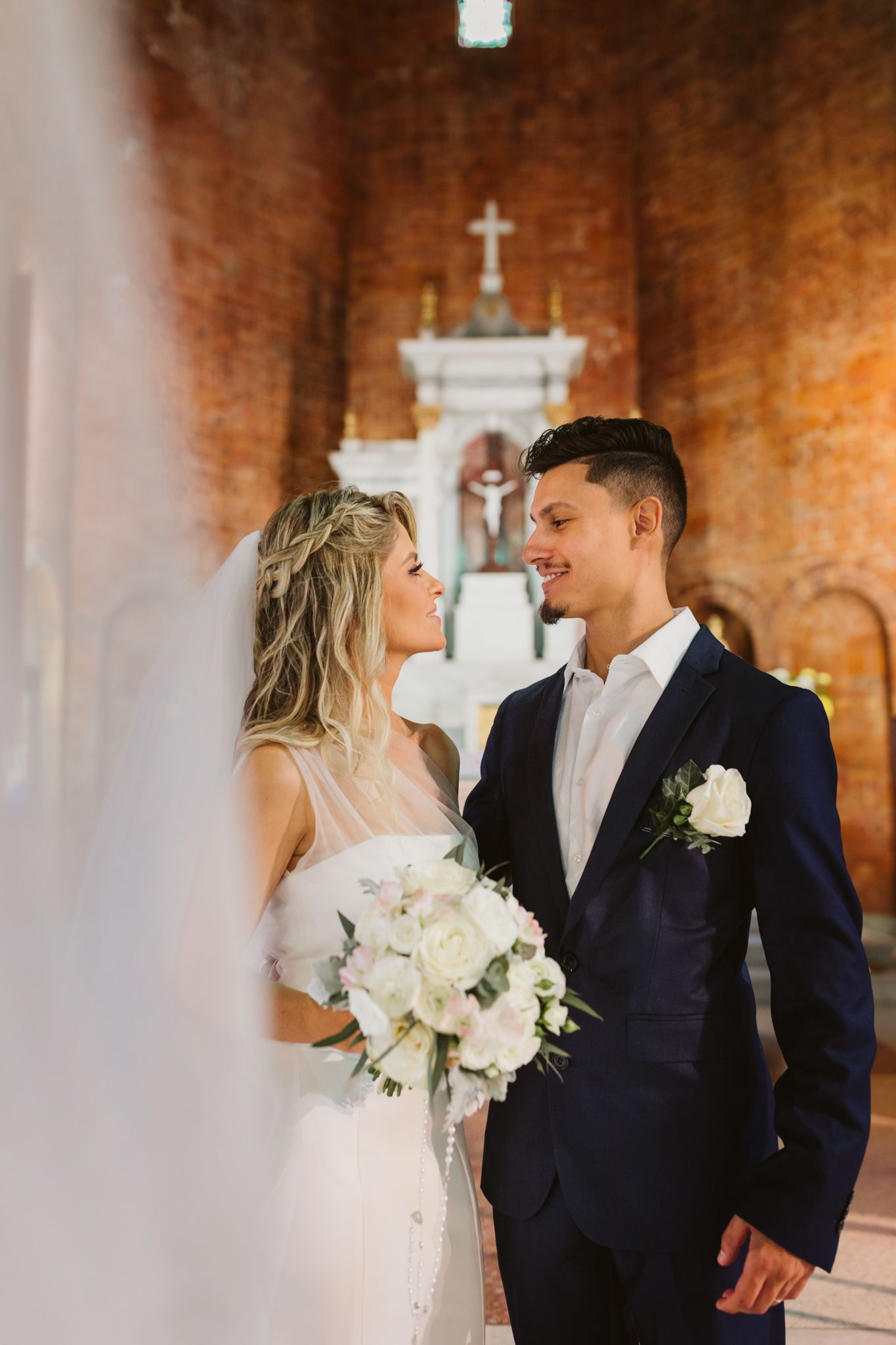 Wedding couple sharing intimate moment in church with brick walls and cross in background.