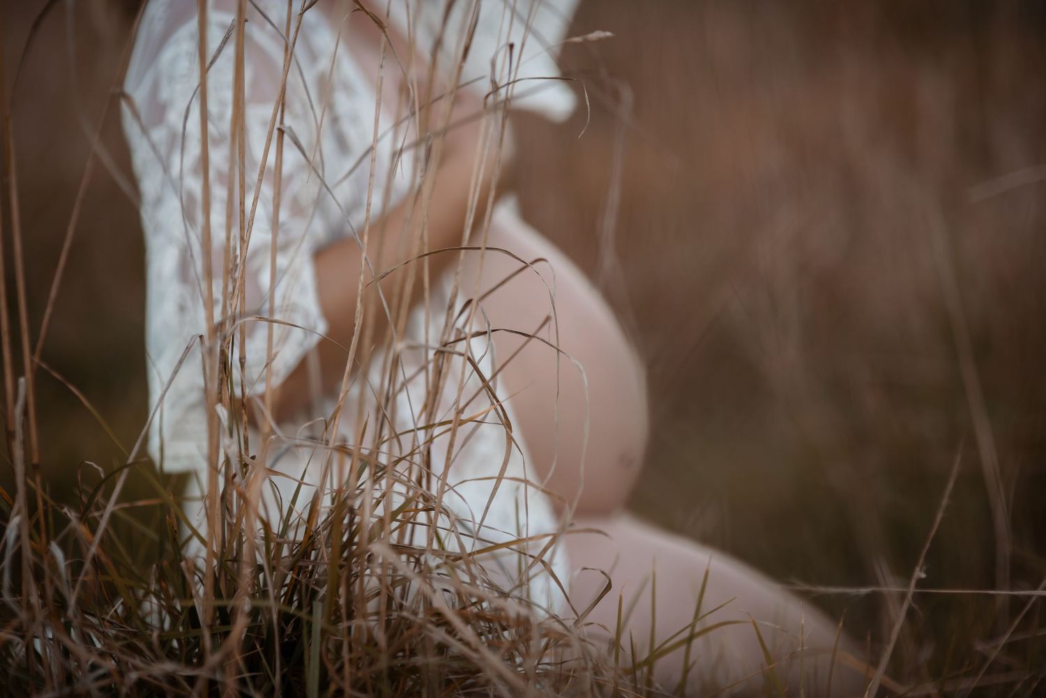 Artistic maternity silhouette through tall grass with soft natural lighting.