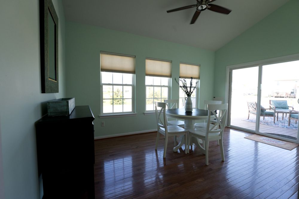 Bright sunlit room with hardwood floors, white trim, and mint green walls featuring a desk and chairs.