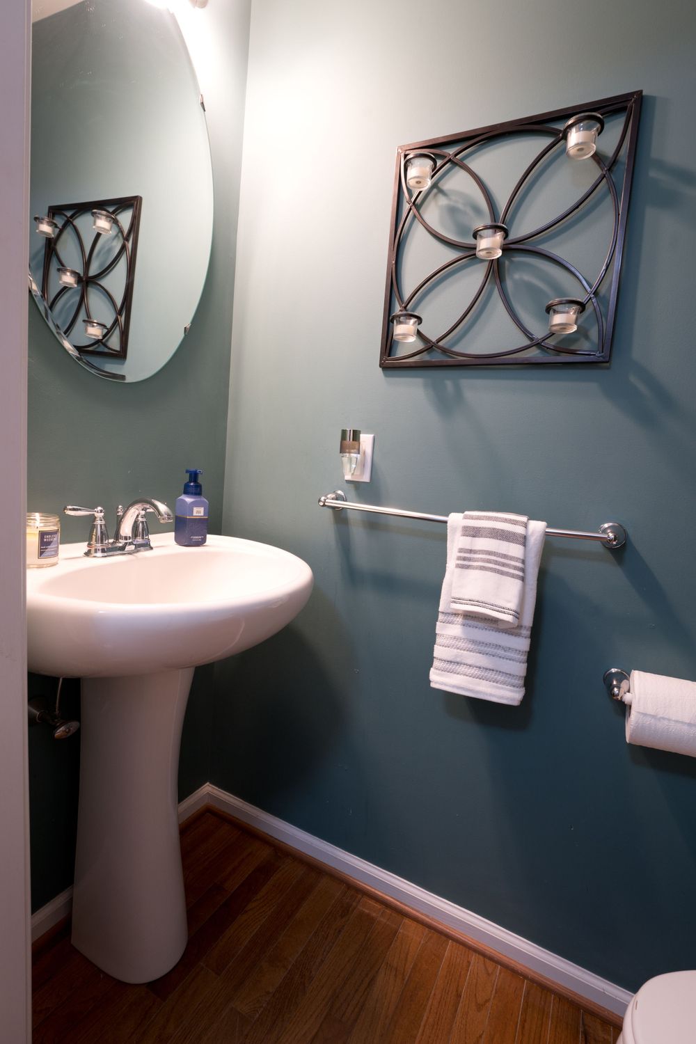 Powder room with pedestal sink, blue-gray walls, and decorative metal wall art above towel bar.