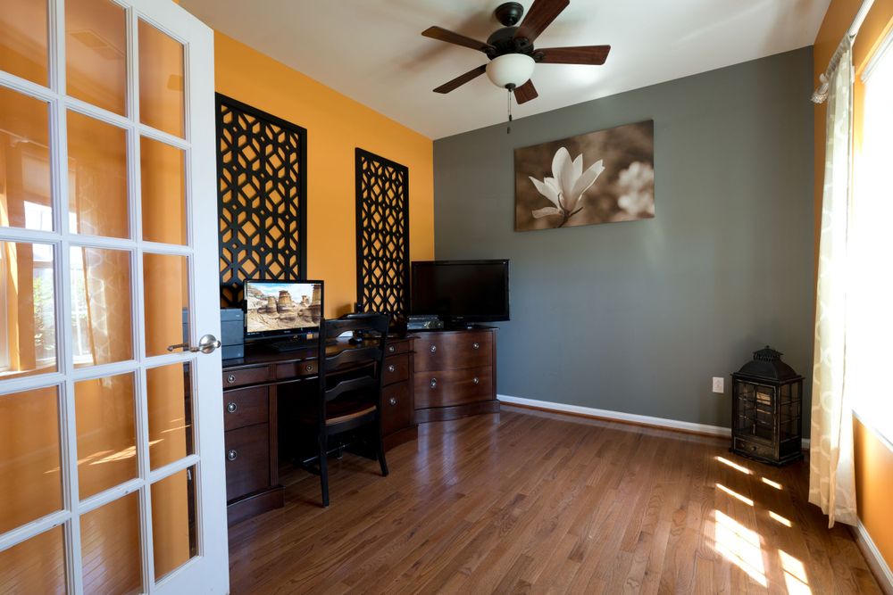 Home office with orange accent wall, French doors, hardwood floors, and decorative wall panels.