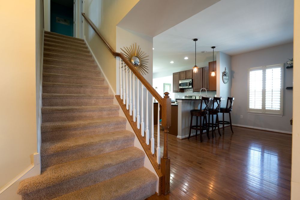 Modern entryway featuring wooden staircase with white railings and open view to kitchen area.
