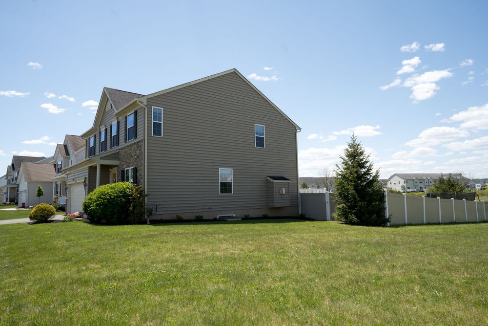 Side view of a beige vinyl-sided house with fenced yard and mature landscaping.