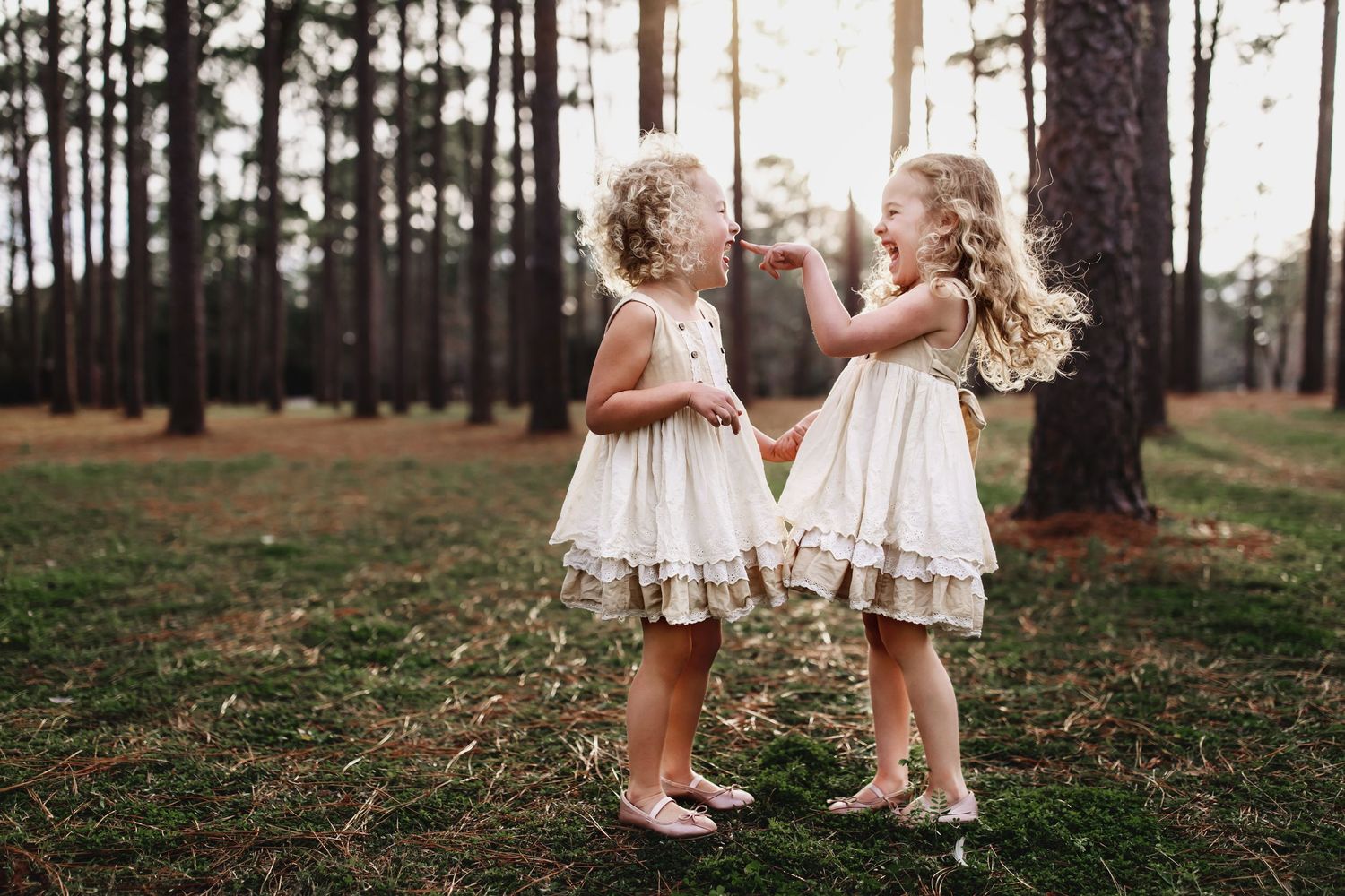 Two small figures in white dresses playing in a pine forest.