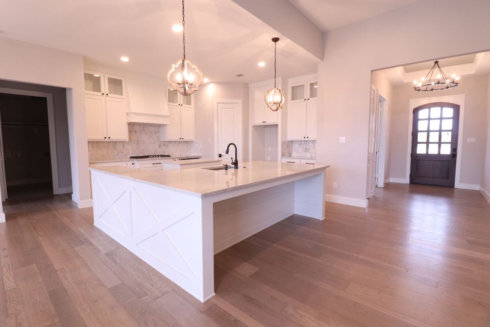 Modern white kitchen with large center island, pendant lighting, and hardwood floors in new home.