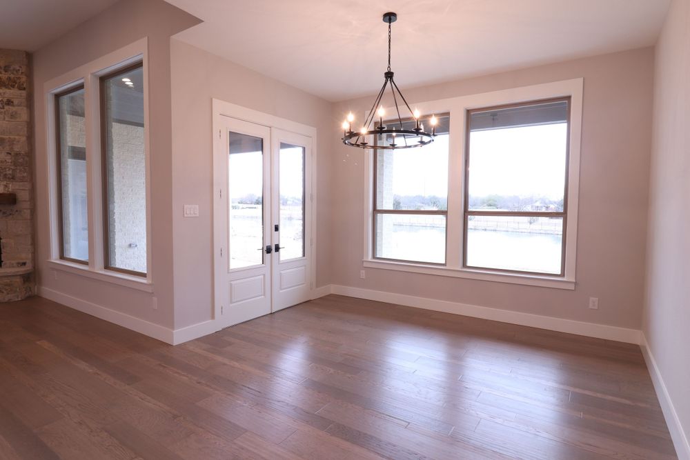 Bright empty dining room with French doors, chandelier, and large windows in a newly built home.