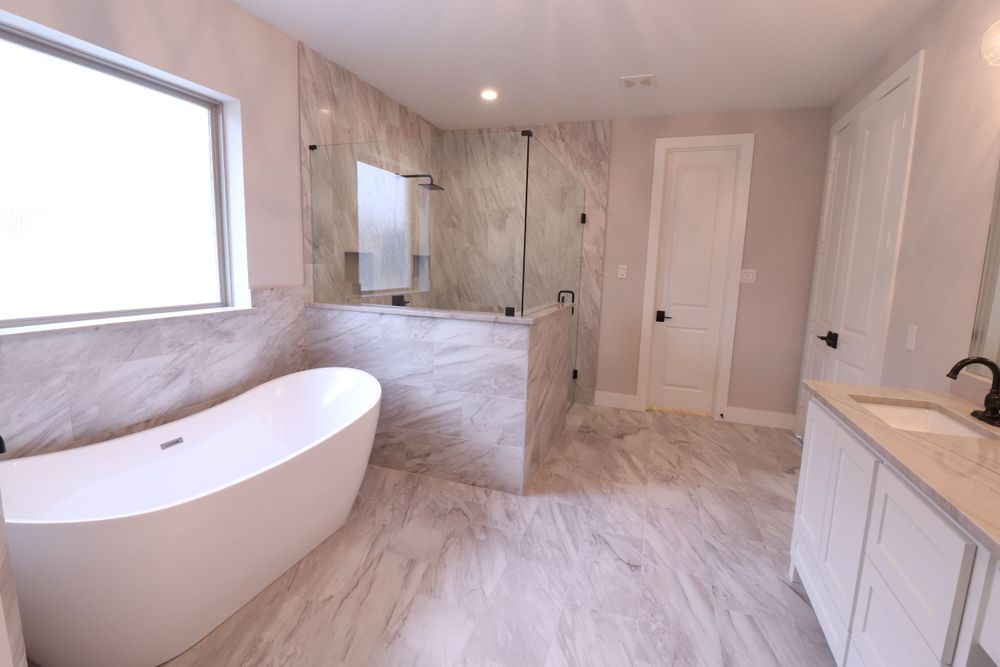 Elegant master bathroom with freestanding soaking tub, marble tile, and glass shower enclosure.