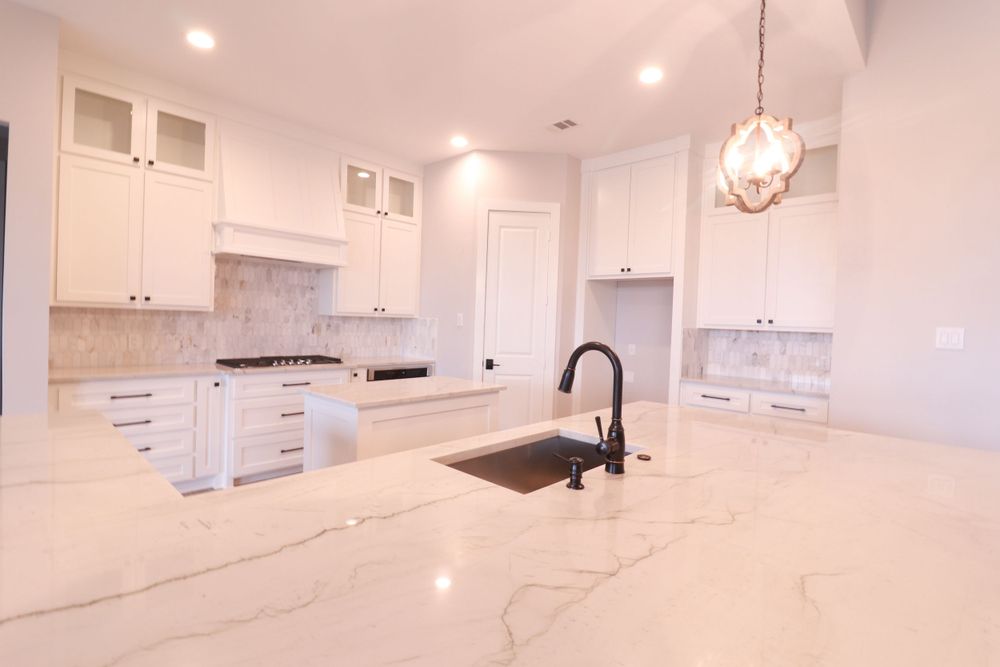 Modern white kitchen with quartz waterfall island, black sink, marble backsplash, and pendant lighting.