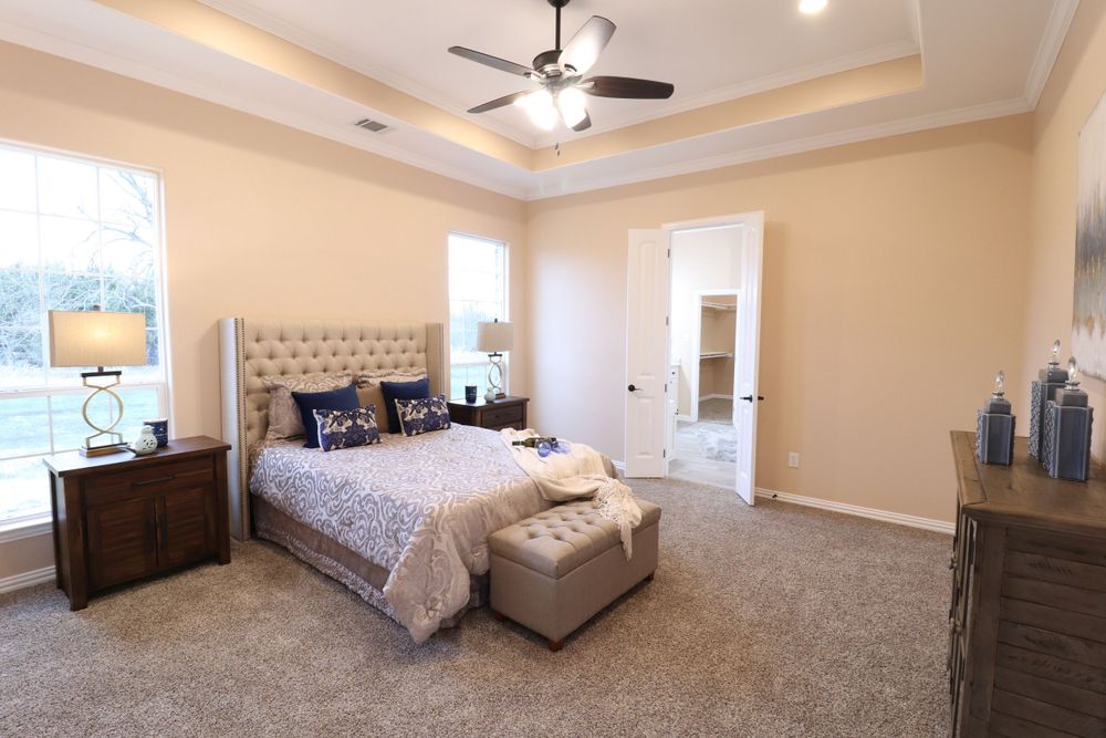 Spacious master bedroom with tray ceiling, ceiling fan, neutral carpet, tufted headboard, and elegant decor.