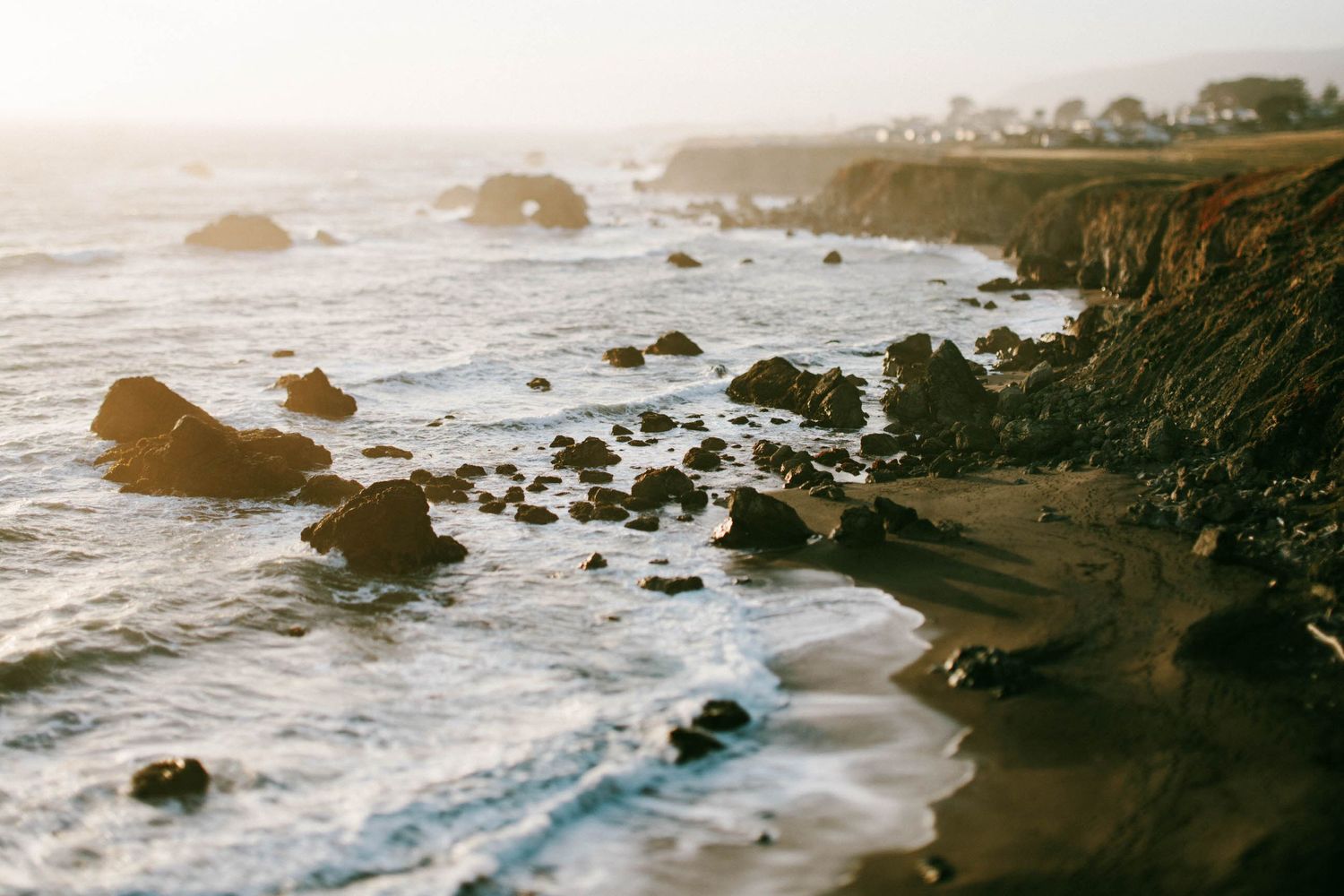 Dramatic rocky coastline with crashing waves and misty cliffs during golden hour.