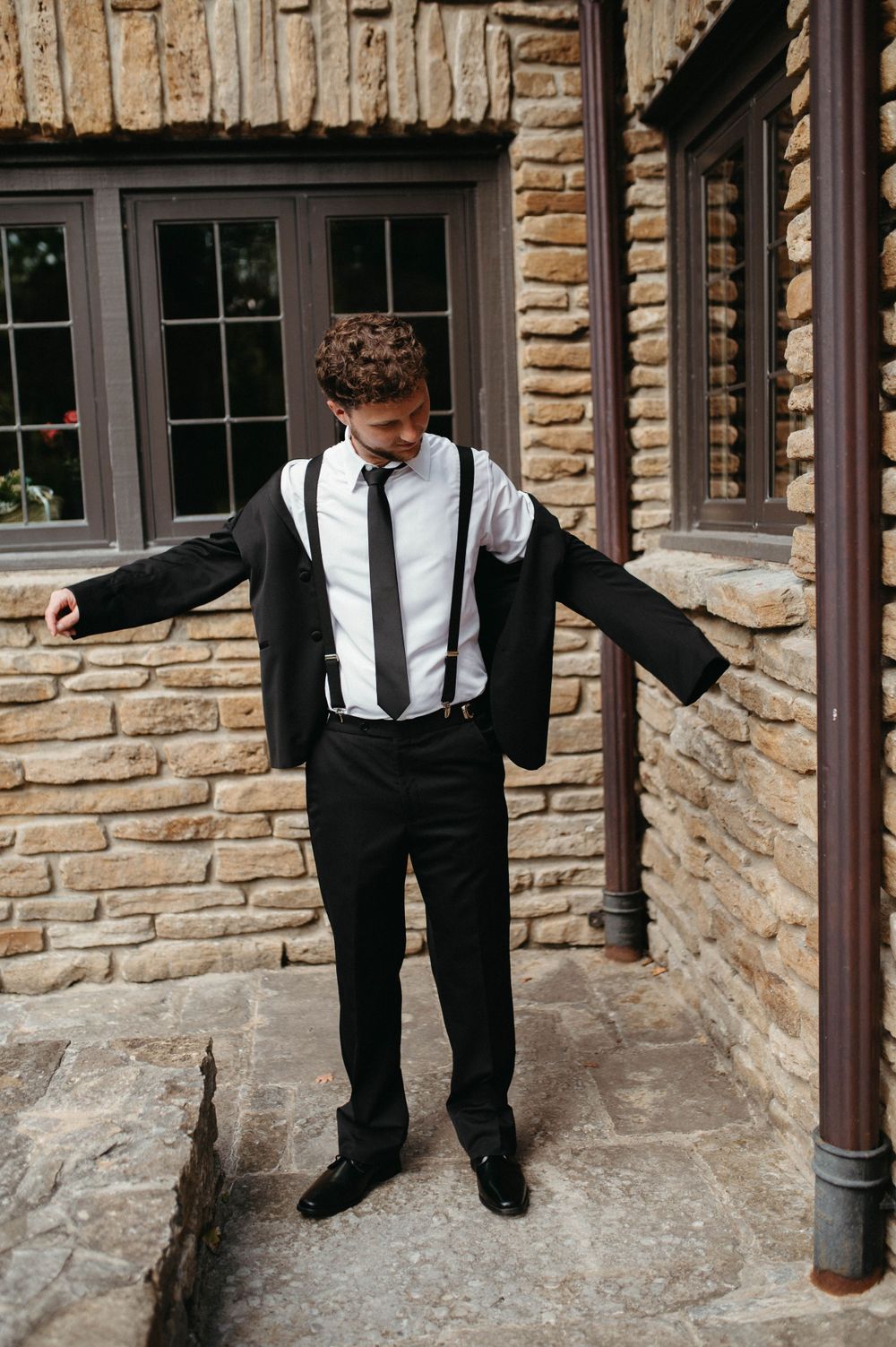 A formal suit with suspenders and tie against a stone building backdrop.