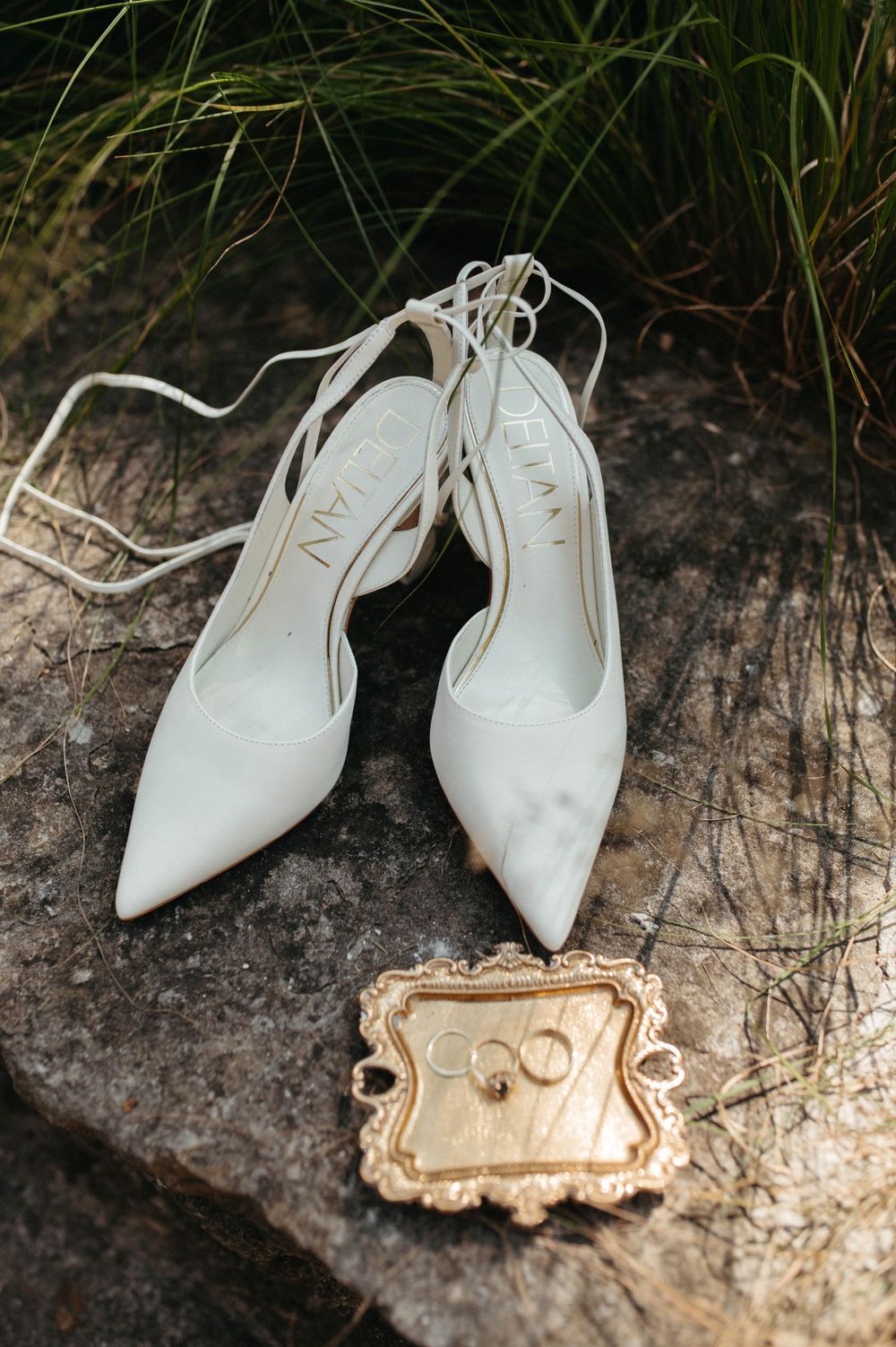 White bridal heels and ornate gold tray placed on rustic stone surface outdoors.