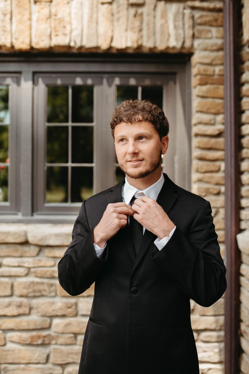 Classic black suit and tie formal attire against stone building exterior.