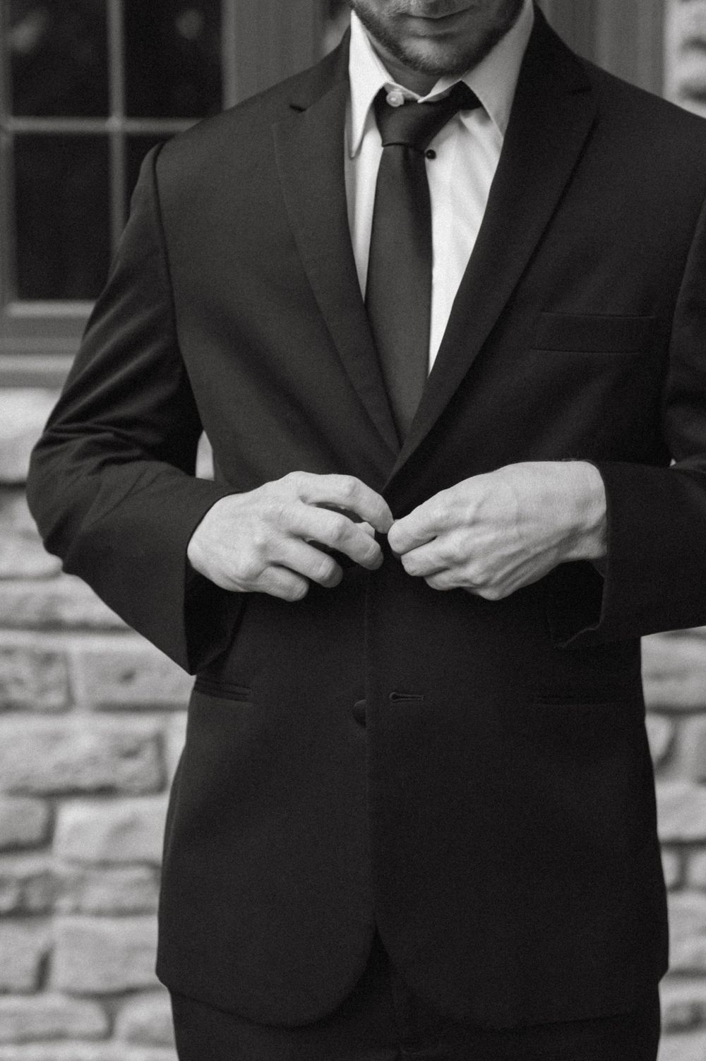 Close-up of hands adjusting buttons on classic black suit jacket.