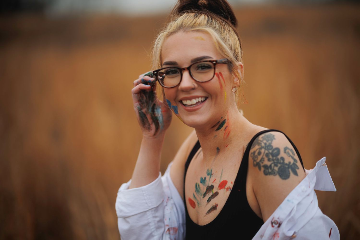 A candid portrait showing tattoos and glasses while talking on phone at sunset.