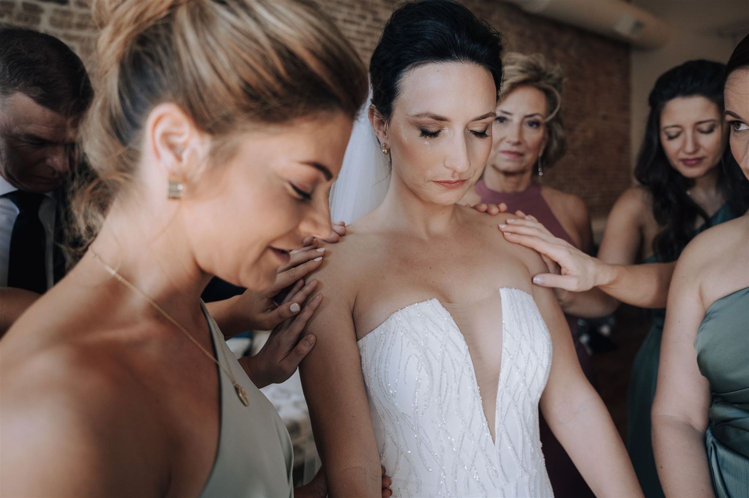 Bridesmaids in soft pastel dresses helping with final wedding dress adjustments.