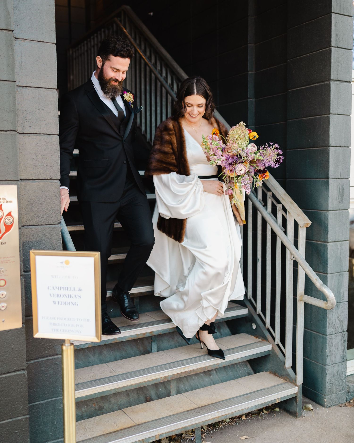 Wedding party exiting venue down concrete steps with directional signage.