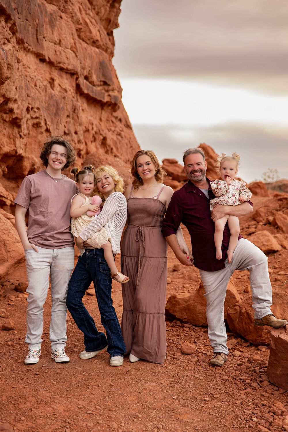 A family poses together against stunning red rock formations in a desert landscape during sunset.