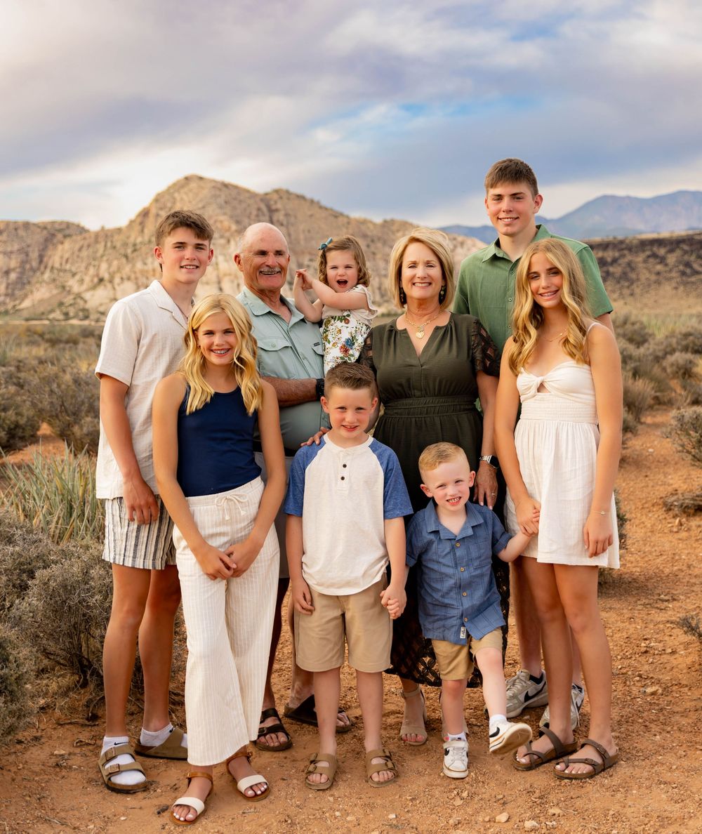 A family poses together on a desert trail with mountains and sagebrush in the background during golden hour.