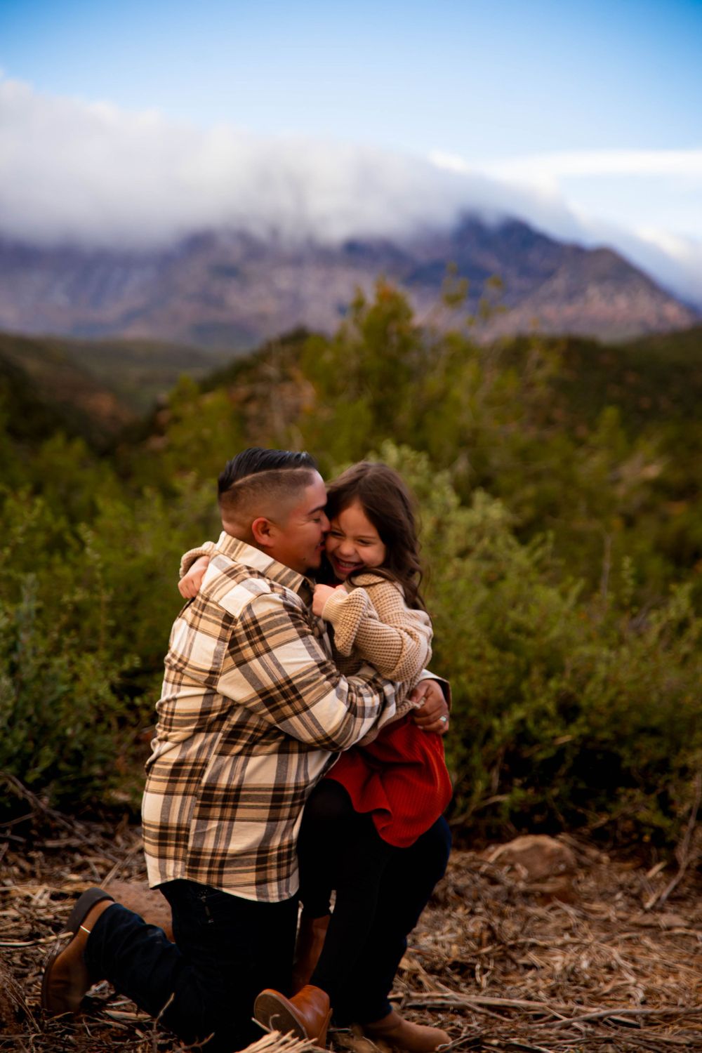 A sweet embrace captured outdoors with dramatic mountain scenery behind.