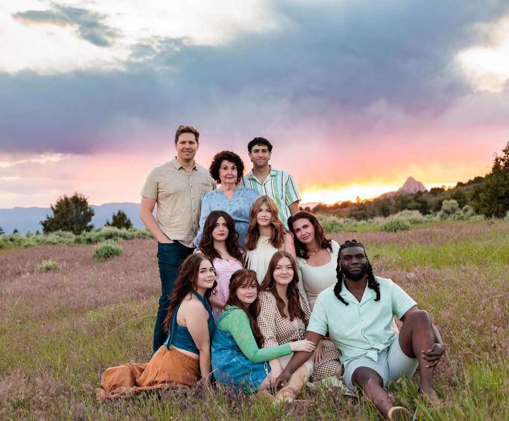 A diverse group of ten people posing together in a field at sunset with mountains in the background.