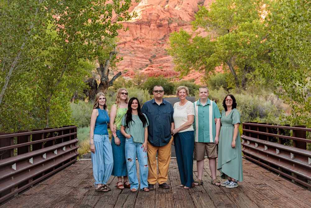 Family group photo on a wooden bridge with red rock canyon and green trees backdrop.
