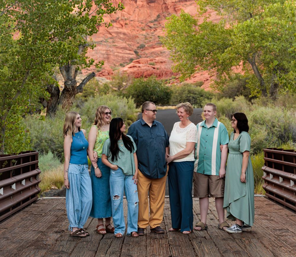 Family portrait on a wooden bridge with red rock canyon and green trees in the background.
