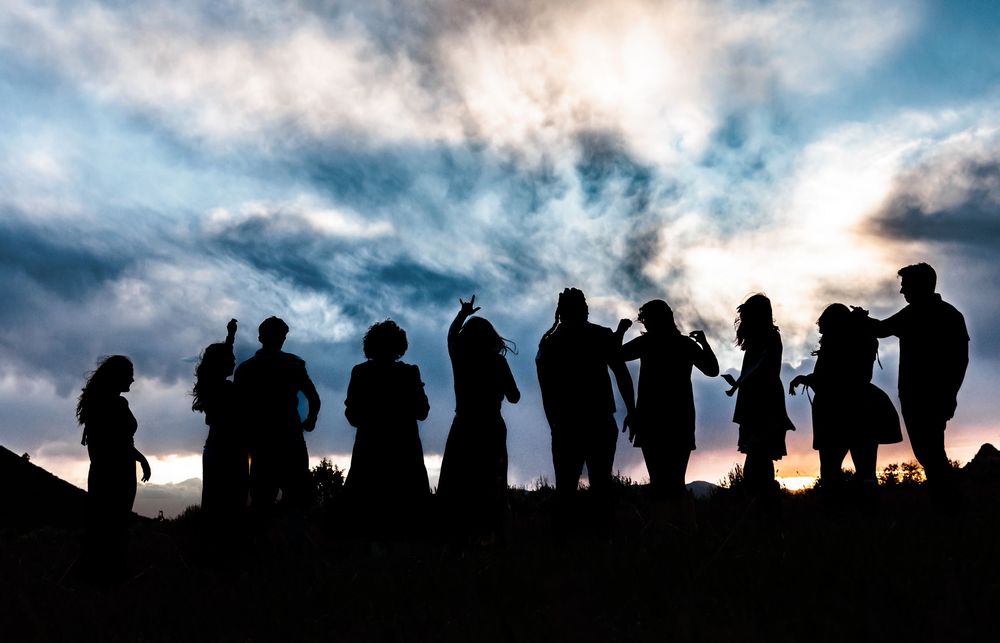 Silhouettes of a group of people gathered on a hill at sunset with dramatic cloudy sky.