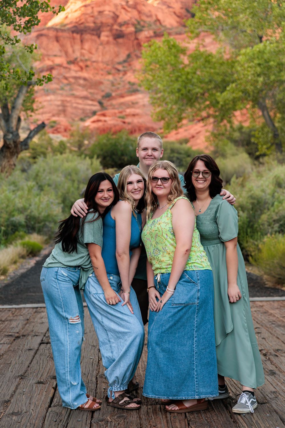Five people posing together on a wooden path with red rock canyon and green trees in the background.